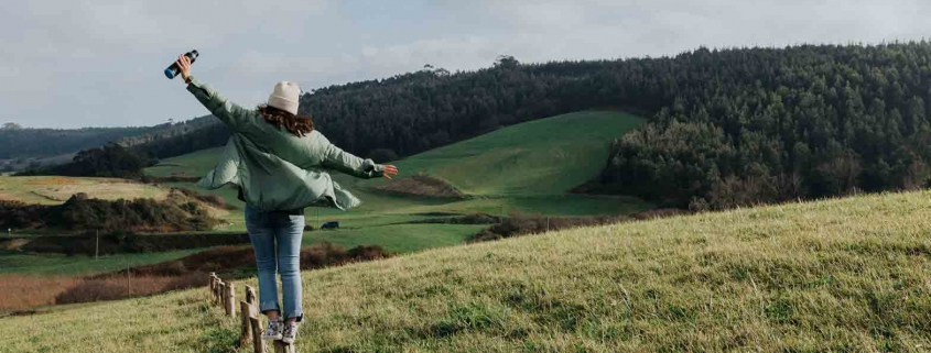 Frau balanciert auf Wiese. Warum leben wir nicht so nachhaltig wie wir wollen?